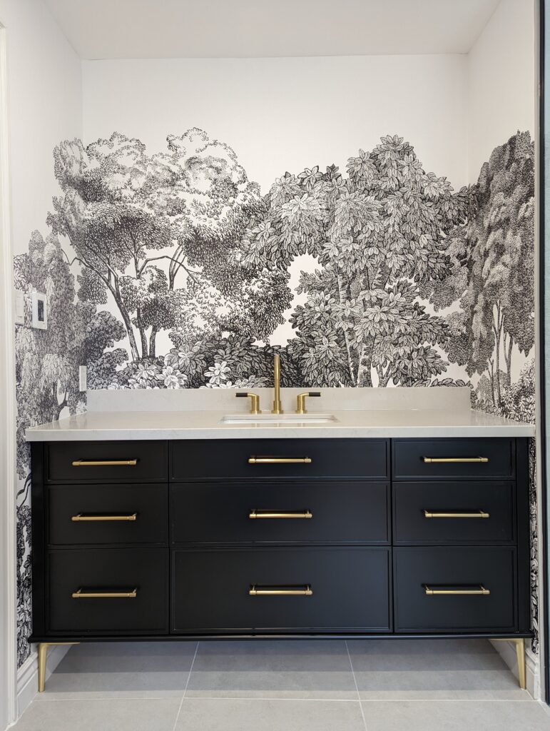 A stunning wallpaper mural behind a vanity sink, displaying large, leafy trees in black and white.