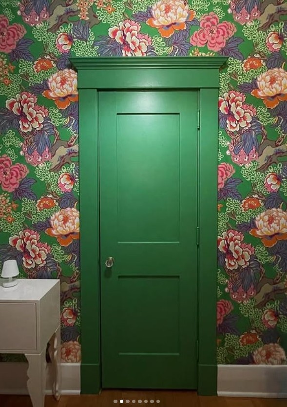 A green door displayed against interesting printed wallpaper that is showing a funky print of green lilypads and pink lillies.
